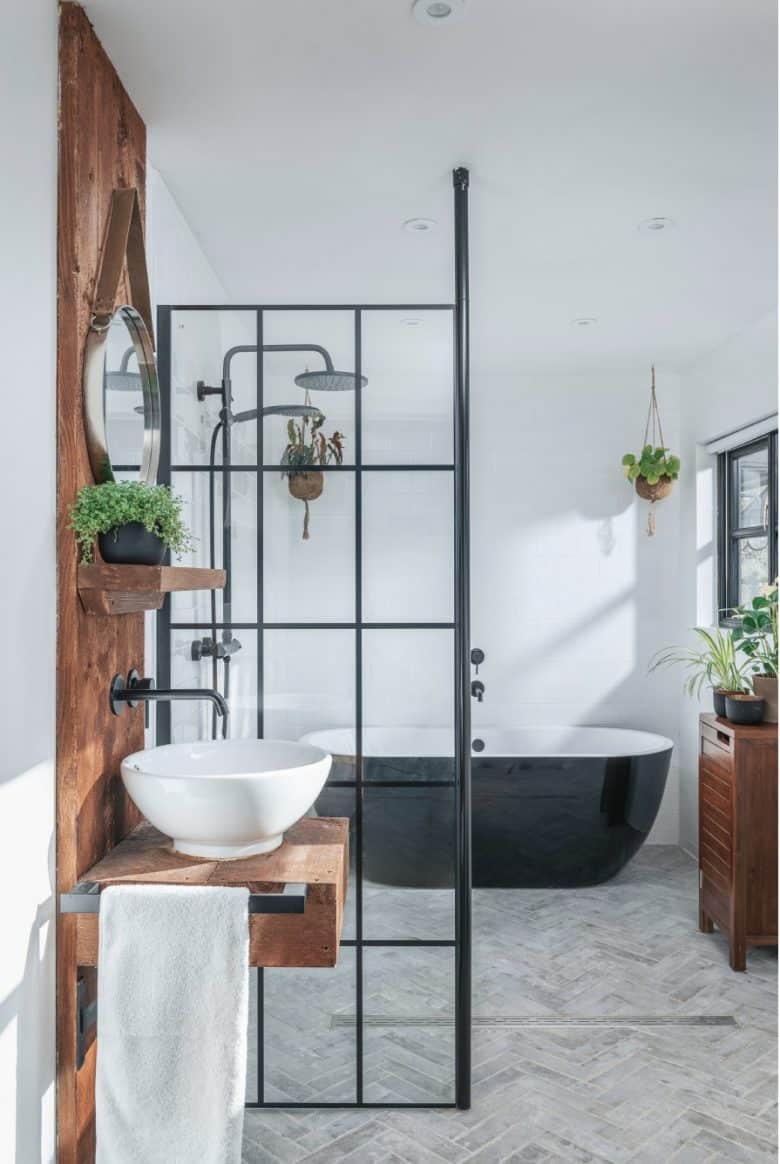 modern rustic bathroom interior with white walls, herringbone tile floor wet room with reclaimed wood splasback panel and white wash bowl with black frame shower panel black taps and shower 