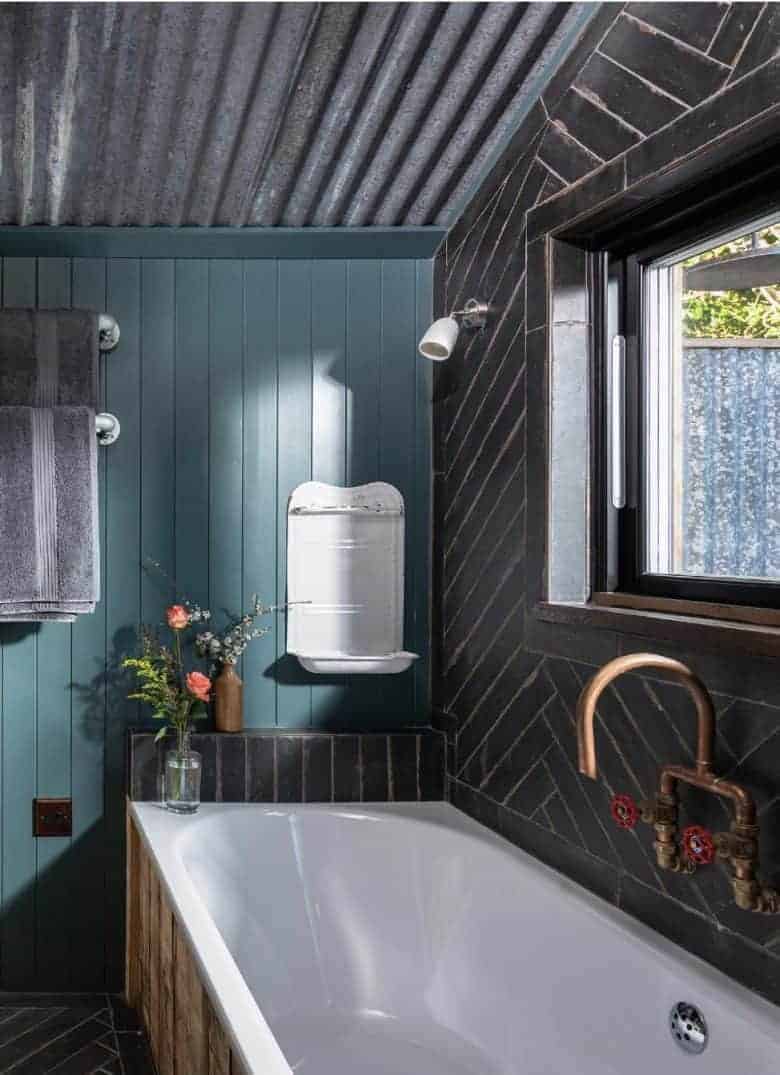 modern rustic bathroom decorating idea combining dark teal tongue and groove wall panelling with reclaimed brass industrial taps, vintage enamel soap holder corrugated metal roof and reclaimed wood panelling on the bath #modern #rustic #bathroom #reclaimed #vintage