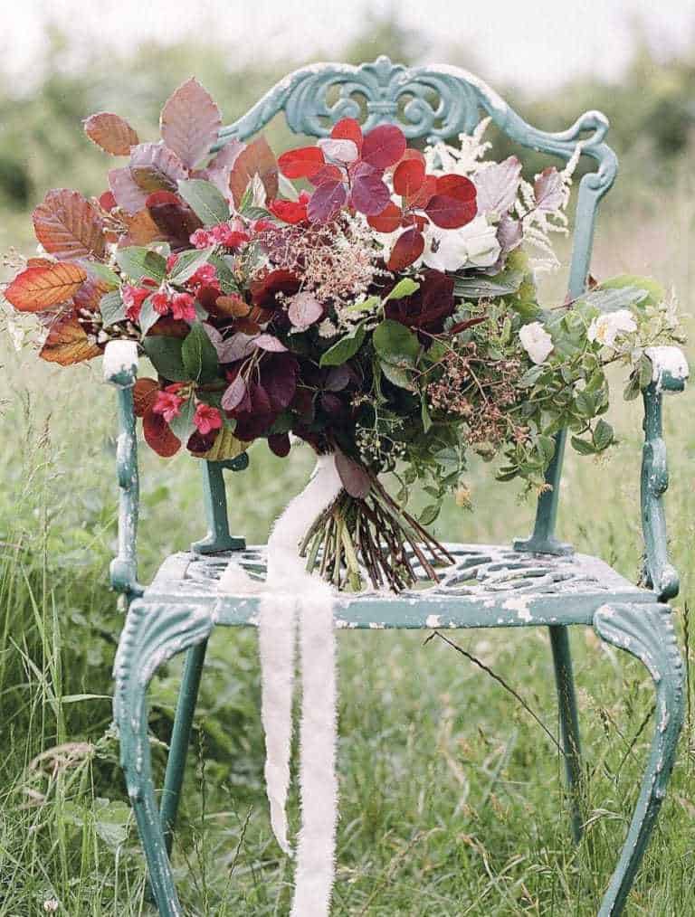 love this seasonal autumn flower arrangement on vintage metal chair using berries, autumn leaves, foraged greenery and flowers. #frombritainwithlove #mybritainwithlove #britishflowers #autumnflowerideas #autumnleaves