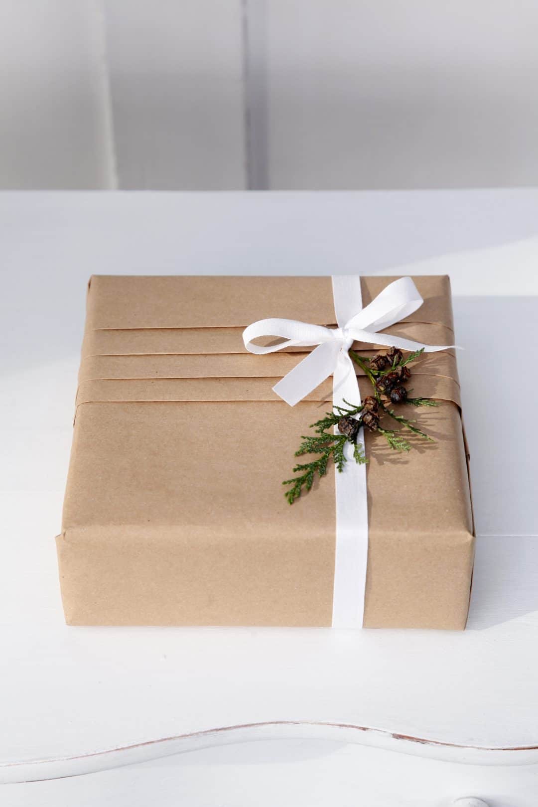 love this idea of pleating brown kraft paper as christmas gift wrap with white ribbon and fresh green foliage by jane means. Click through to find out more and get other ethical and plastic free christmas gift wrap ideas you'll love to try