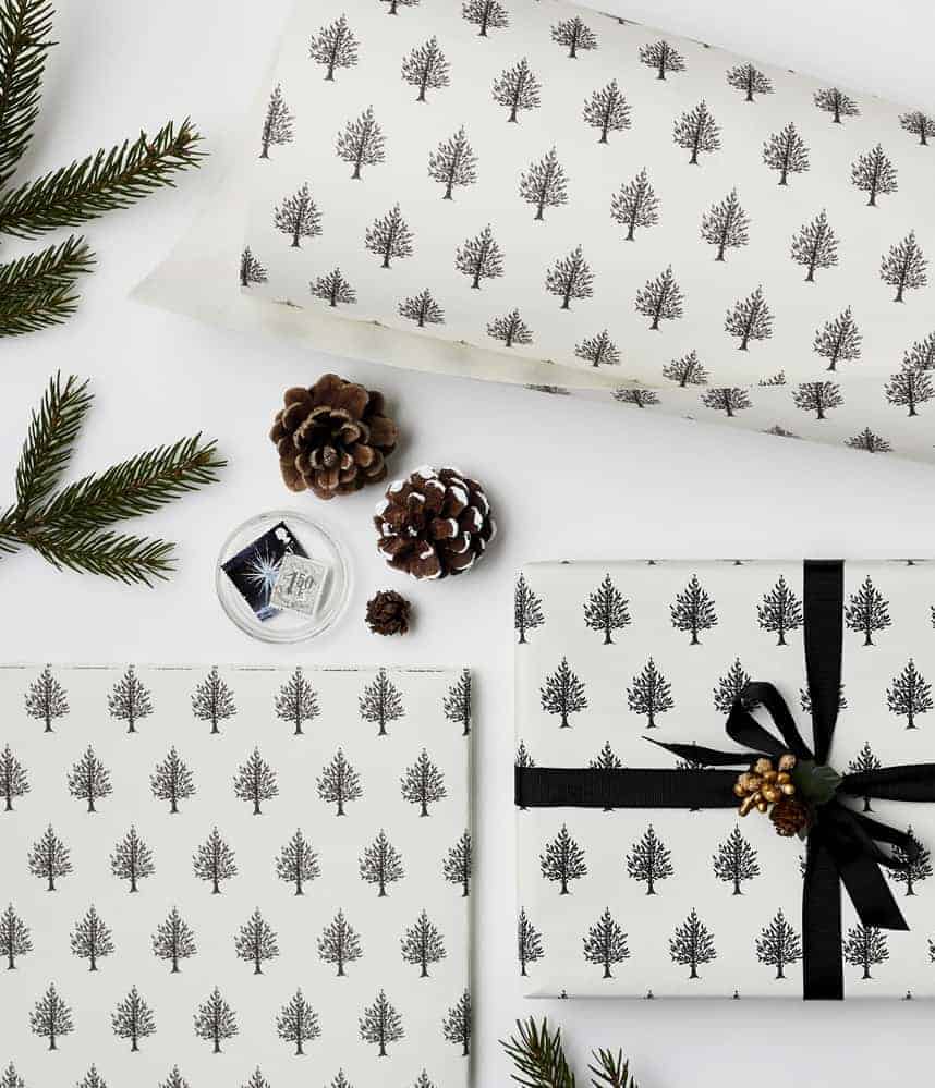 love this simple black and white christmas tree print scandi gift wrap with black ribbon fresh foliage and pine cones by katie leamon. Click through for more ethical eco-friendly and plastic free christmas gift wrapping ideas you'll love to try