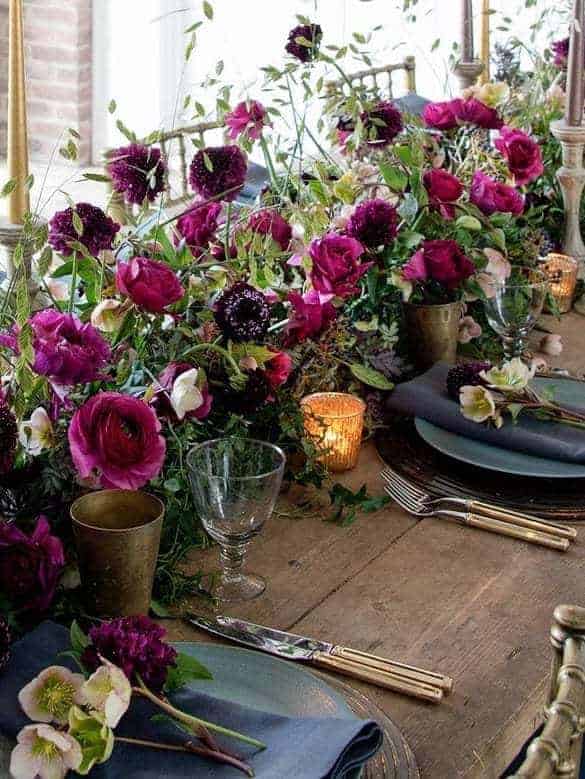 love this christmas flower arrangement using dark red and purple roses with lime white hellebores and rustic wooden table and brass with candles. Click through for more DIY christmas flower centrepiece ideas you'll love to try this holiday season