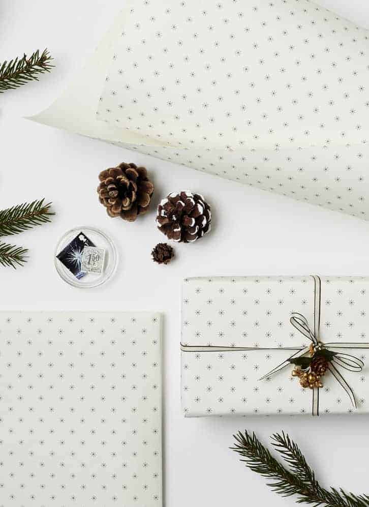 love this simple black and white christmas snowflake print scandi gift wrap with black ribbon fresh foliage and pine cones by katie leamon. Click through for more ethical eco-friendly and plastic free christmas gift wrapping ideas you'll love to try