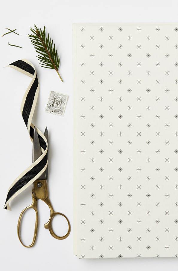 love this simple black and white christmas snowflake print scandi gift wrap with black ribbon fresh foliage and pine cones by katie leamon. Click through for more ethical eco-friendly and plastic free christmas gift wrapping ideas you'll love to try